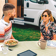 A man and woman sitting at a picnic table near their RV
